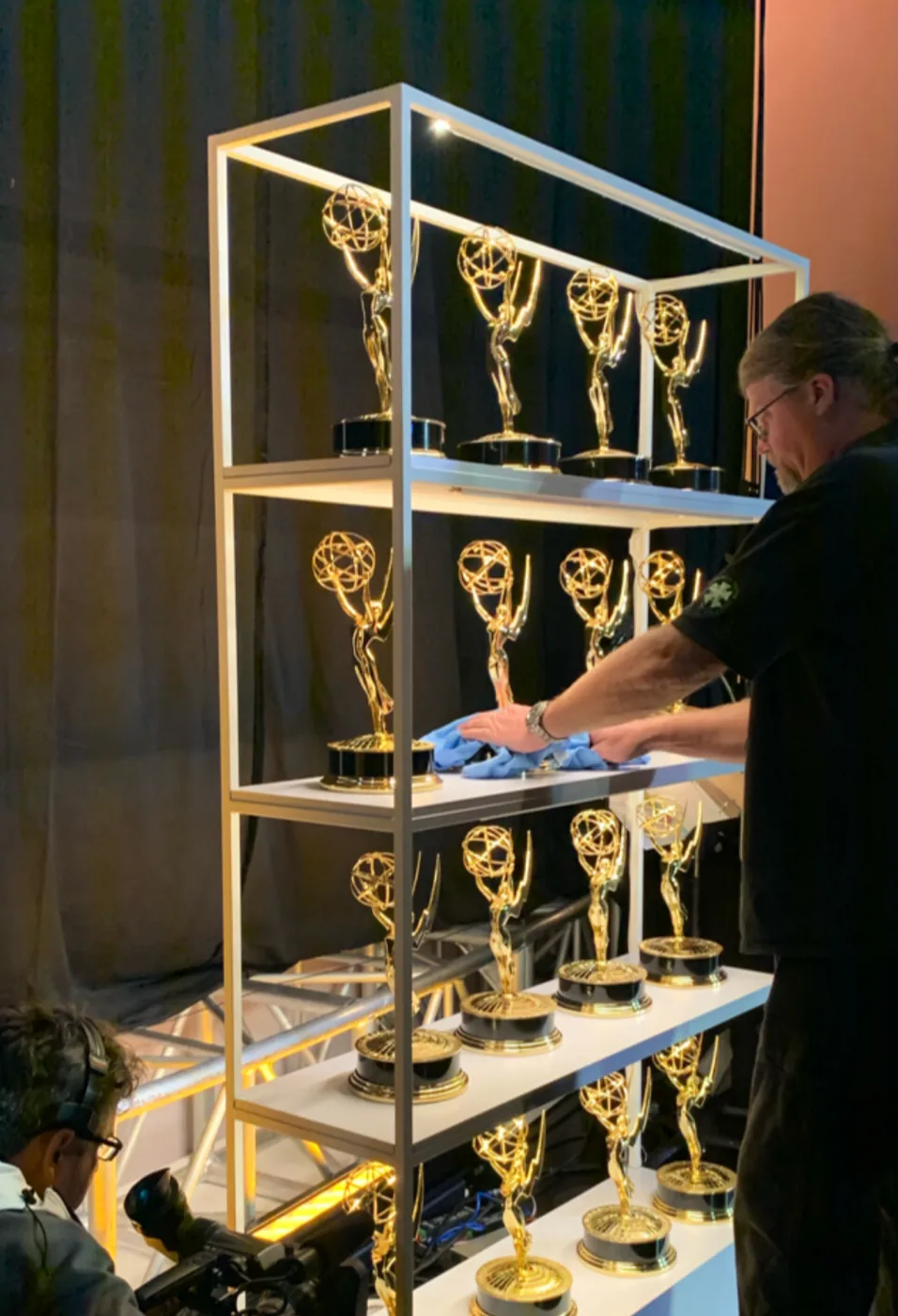 Emmy statuettes on a lit backstage shelf being polished before the show