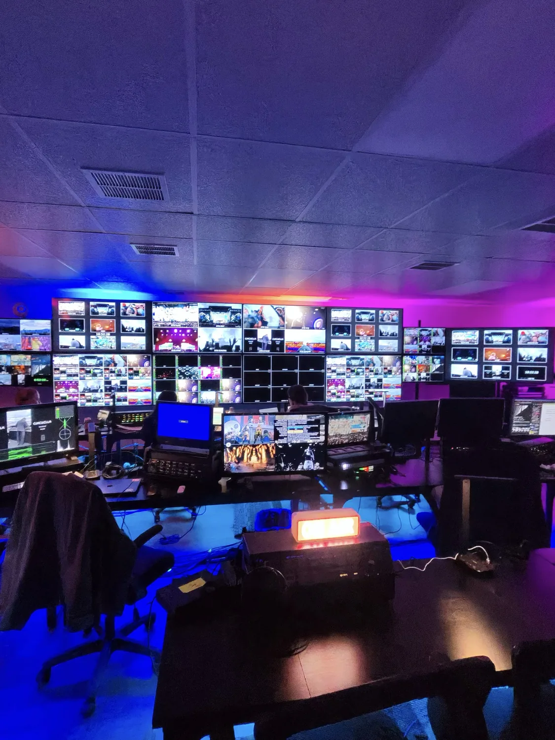A remote control room with walls of multiview monitors lit blue and magenta